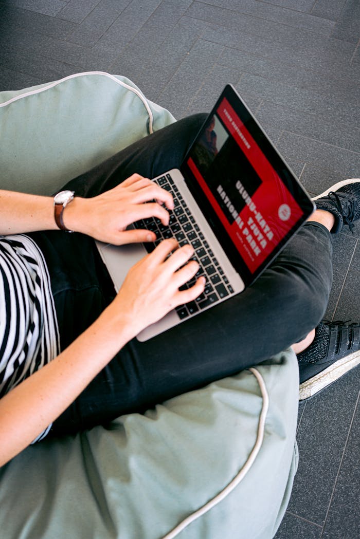 hero-img-01 Person working remotely on a laptop while sitting comfortably on a beanbag chair indoors.